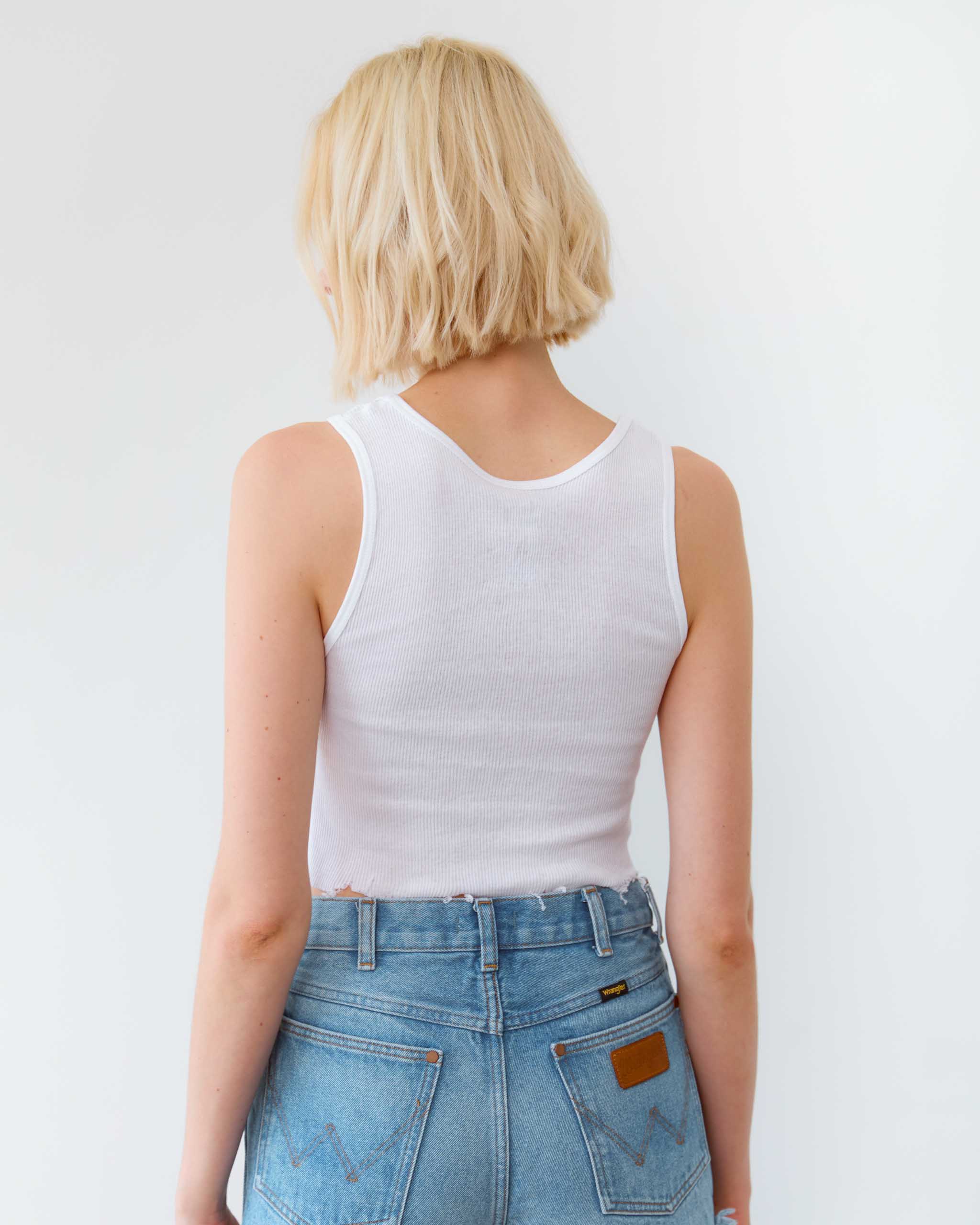 Person wearing a white tank top and blue jeans against a plain background