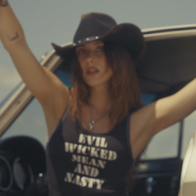 A gothic western cinematic video featuring models wearing Sleazy Rider tank tops and cowboy hats, posing in front of vintage Corvettes and Harley Davidsons.